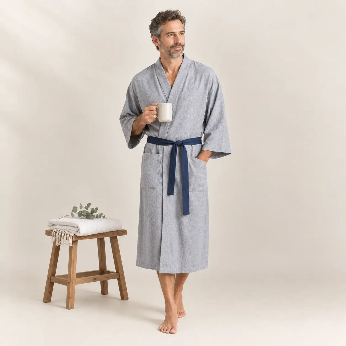 A man wearing a light gray textured cotton male kimono robe with a navy blue belt and two front pockets Image