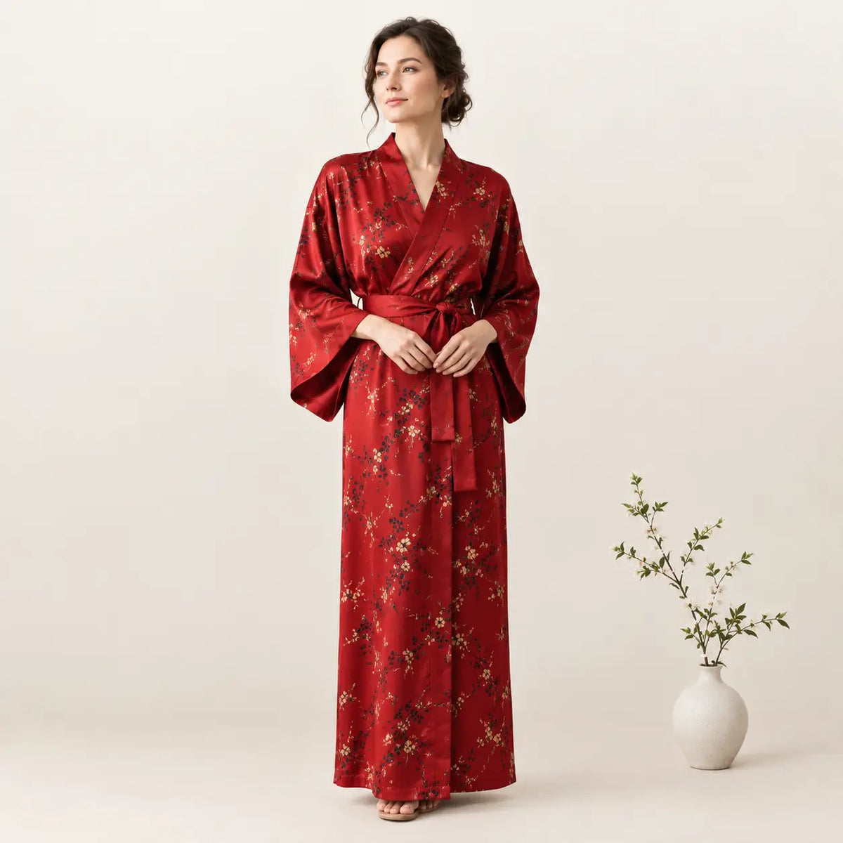 A woman wears a rich red satin kimono robe with delicate gold floral embroidery and wide flowing sleeves. Image