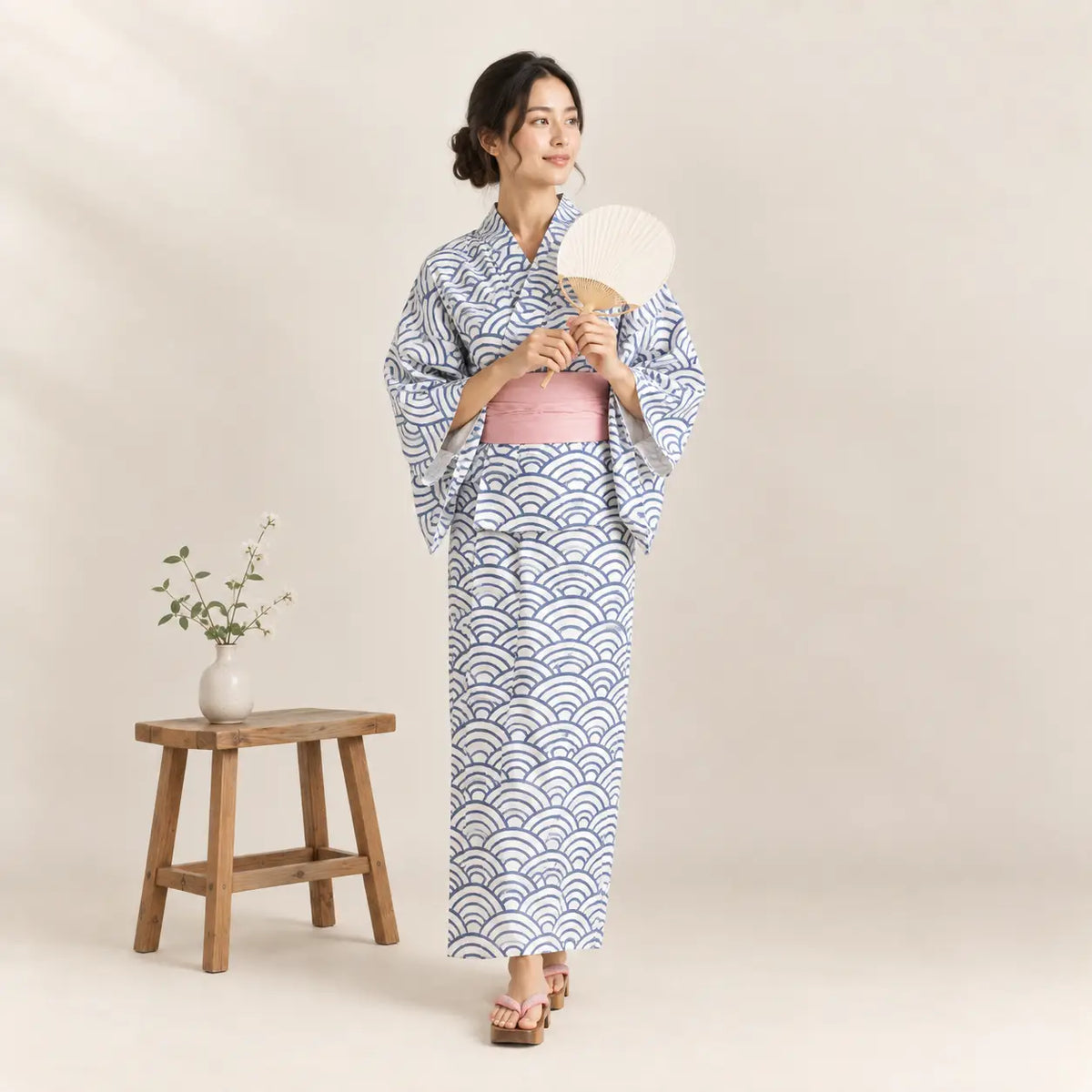 A woman wears a yukata kimono with light blue and white wave patterns and a soft pink obi belt. Image