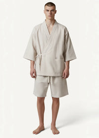 A man wearing beige striped cotton kimono pajamas with tie belt front pockets and matching shorts