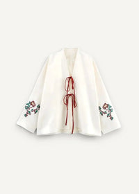 White embroidered kimono jacket with red and green floral sleeve patterns and a matching red front tie