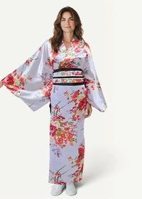 A woman wears a white satin floral kimono with red and pink patterns and a black obi belt in a traditional style