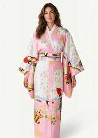 A woman wears a pink and white formal Japanese kimono with traditional motifs wide sleeves and an ornate obi belt
