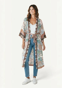 A woman wearing a pastel tropical floral kimono duster cardigan with wide sleeves and a matching belt