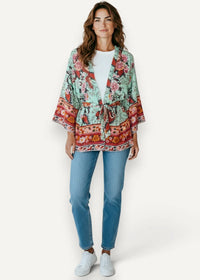 A woman wears a light mint green kimono mini dress with red and pink floral patterns and an embroidered waist belt