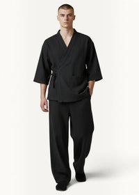 Man wearing black cotton men's kimono pajamas with three quarter sleeves and a tied waist
