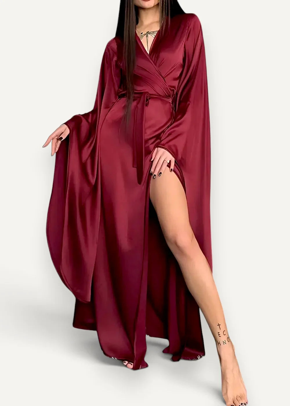 A modern kimono dress in deep burgundy satin with wide sleeves and a high slit flowing gracefully
