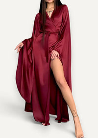 A modern kimono dress in deep burgundy satin with wide sleeves and a high slit flowing gracefully
