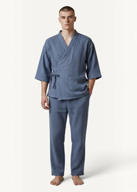 A man wearing navy men’s kimono pajamas in blue textured cotton with matching pants and a tied belt