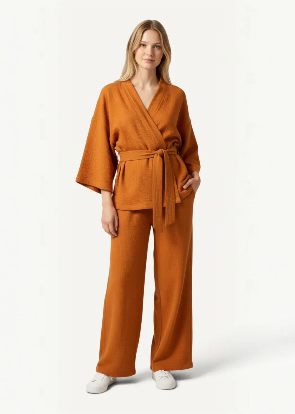 A woman wears orange kimono pajamas featuring a rust-colored loose wrap jumpsuit with wide-leg trousers and bell sleeves