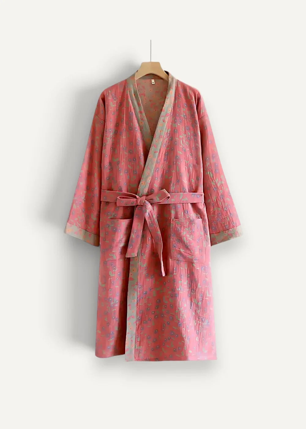 A soft pink kimono robe with a subtle floral pattern and matching belt hanging on a wooden hanger