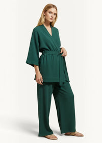 A woman wearing deep emerald green ribbed knit teal kimono pajamas with wide sleeves and high-waisted waist tie trousers