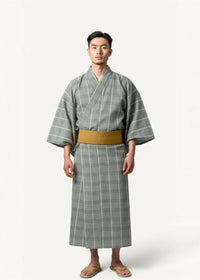 A man wearing a gray and white plaid yukata with a mustard-yellow obi belt in a traditional Japanese male kimono style