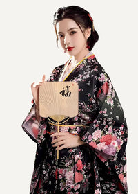 Woman wearing a black floral yukata robe and holding a traditional Japanese hand fan