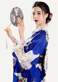 A woman wearing a vibrant blue and white silk floral embroidered yukata holding an ornate bird and cloud hand fan