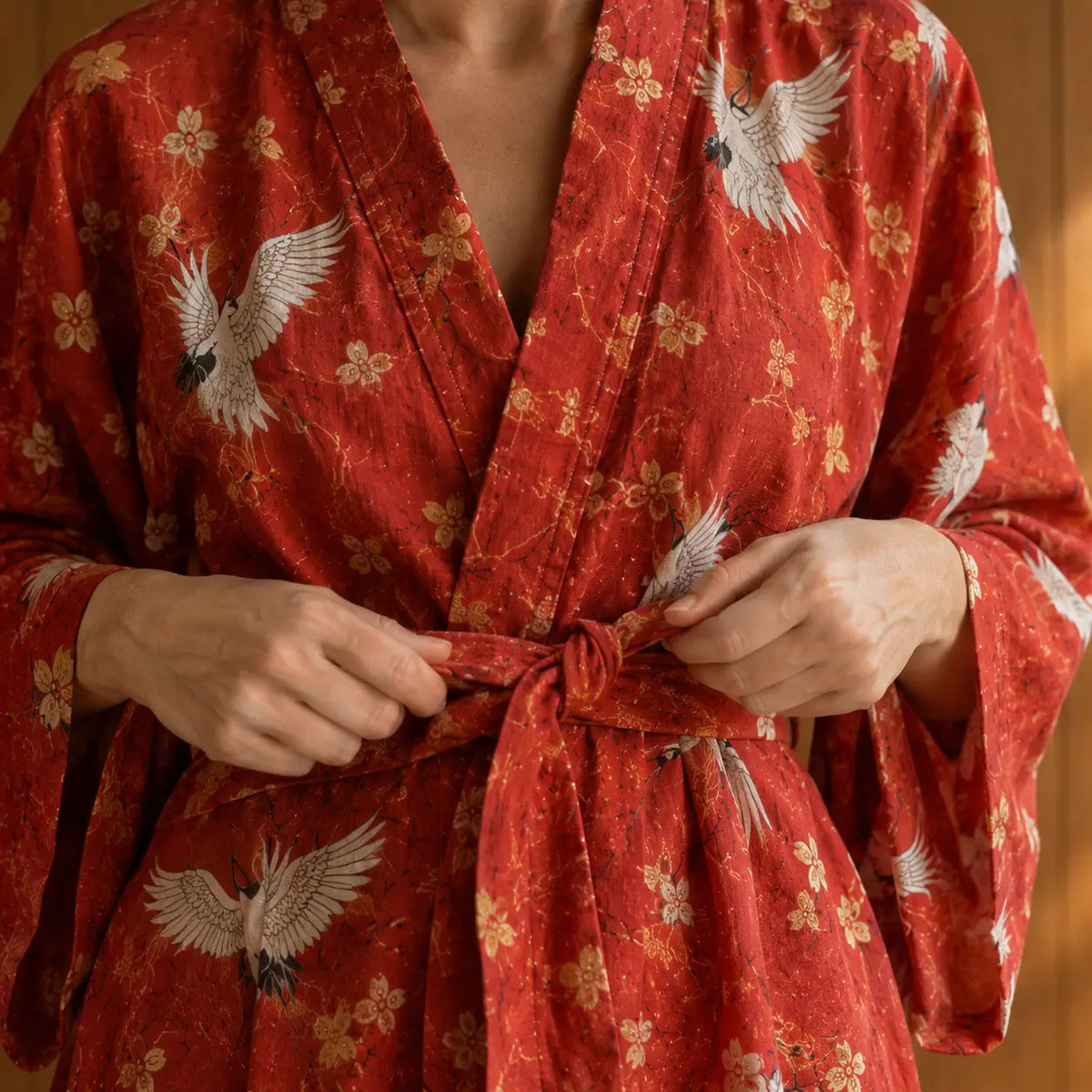 Woman tying the belt of a red kimono robe with white cranes Image